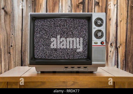 Vintage portable television on old table with wood wall and static screen. Stock Photo