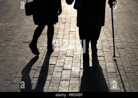 Girl and woman with a cane, black silhouettes and shadows of two people walking on the street. Concept of limping, old age, elderly or blind person Stock Photo