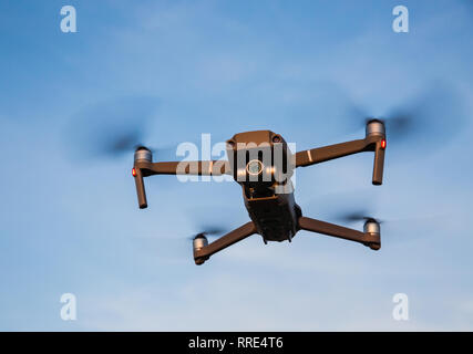 A low angle view of a futuristic drone quadcopter in flight with four propellers turning and drone hovering against a blue sky background Stock Photo