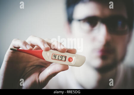 Man holds a red fever thermometer with high temperature in his hand, blurry face Stock Photo