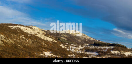 Panoramic view of distant snow capped rocky summit and colorful forest in the winter wonderland below blue sky Stock Photo