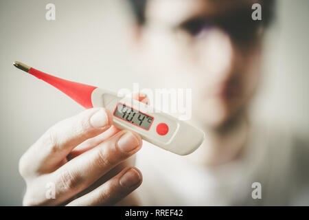 Man holds a red fever thermometer with high temperature in his hand, blurry face Stock Photo