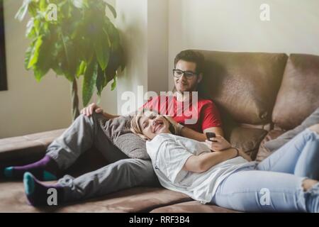 Cheerful man and Woman lying and sitting on sofa while holding remote controller and watching TV Stock Photo