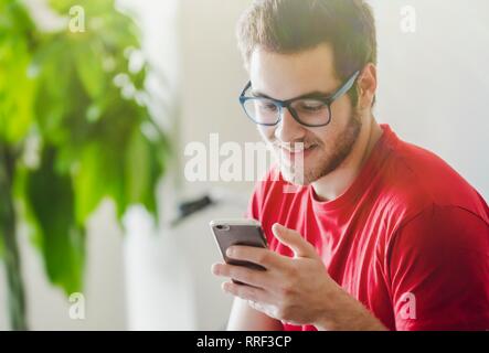 Young handsome bearded man in glasses on the smartphone at home Stock Photo