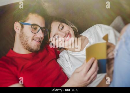 Cheerful dreamy man and Woman lying on couch and reading brochure Stock Photo