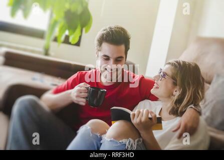 man drinking coffee while sitting on floor with girlfriend reading book Stock Photo