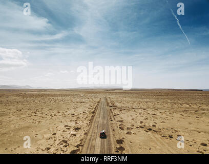 Aerial view of empty desert land with car driving on remote roadway under blue sky, Spain Stock Photo