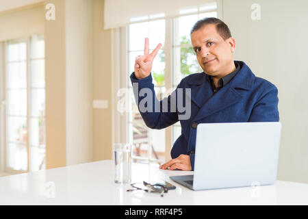 Middle age business man working using laptop smiling with happy face winking at the camera doing victory sign. Number two. Stock Photo