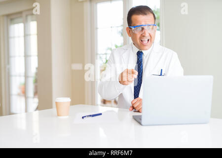 Middle age scientist man wearing professional glasses working using laptop very happy pointing with hand and finger Stock Photo