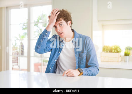 Young handsome man wearing casual denim jacket at home surprised with hand on head for mistake, remember error. Forgot, bad memory concept. Stock Photo