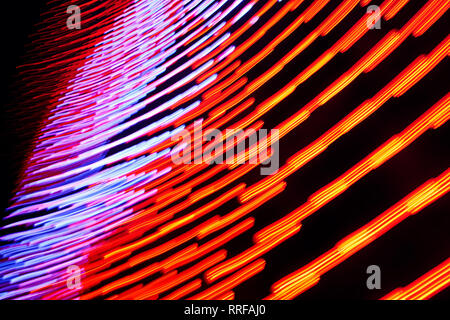 Red-orange and blue-purple glowing lines in motion on the dark background. Closeup horizontal photo. Stock Photo