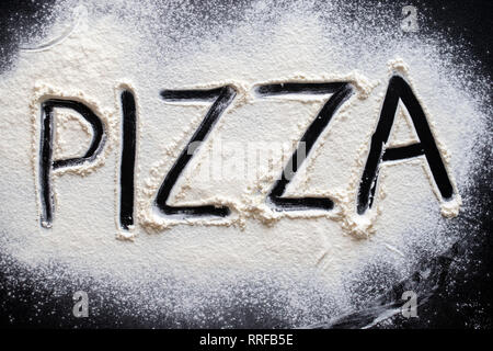 Pizza word written in flour on black table Stock Photo