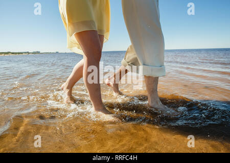 A young couple is having fun and walking on the sea water. Legs close up. Romantic date on the beach. Stock Photo