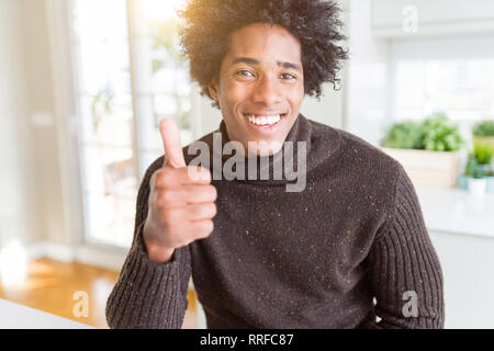 African American man wearing winter sweater doing happy thumbs up gesture with hand. Approving expression looking at the camera showing success. Stock Photo