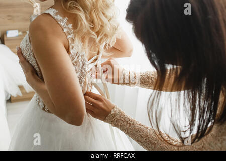 Bridesmaid ties a wedding lace dress to the bride. Stock Photo