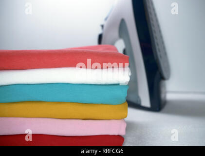 pile of ironed clothes and iron on white background Stock Photo