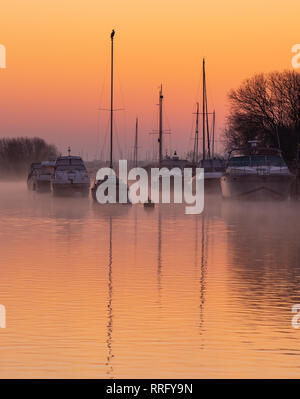 Wareham, Dorset, UK. 26th February 2019. UK Weather: The sky glows with orange and pink hues as the mist rises over the River Frome on a crisp, chilly February morning. A tranquil scene as sailing boats moored along the river bank are reflected in the calm water on the start of what is set to be another gloriously sunny day.  Credit: Celia McMahon/Alamy Live News Stock Photo