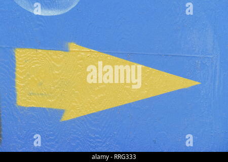 Yellow arrow, direction sign, blue background, painted on wall Stock Photo