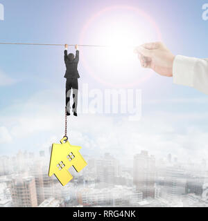 Businessman shackled by gold house hanging on the rope with big hand holding. Stock Photo