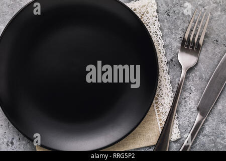 Empty ceramic plate black color with a fork and a knife on a table, top view. Food background Stock Photo