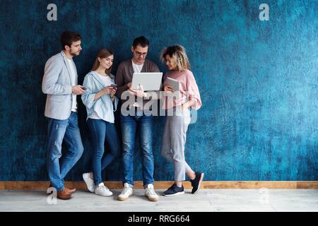 The connected team is an efficient team. Group of businesspeople using wireless technology together while standing in line against a blue background Stock Photo