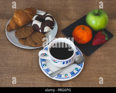 A coffee cup and a plate of black slate with a green apple, a tangerine and a strawberry and one plate with one croissant, one chocolate donut and coo Stock Photo