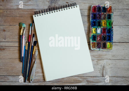 Creative artist workplace flat lay, mockup. Top view on table with blank sketchbook, paintbrushes and dye palettes. Art, workshop, painting, drawing,  Stock Photo