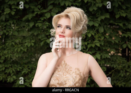 Portrait of beautiful young woman thinking, hand on cheeks, and looking upwards. Bride in golden dress. The concept of perception and reflection Stock Photo