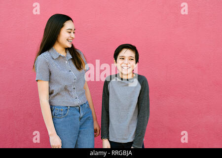 Brother and sister are having a fun time laughing and smiling while standing against the wall Stock Photo