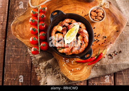 Fried large shrimp in tomato sauce with olive oil, garlic, cilantro and soy sauce, next ingredients for cooking, on wooden background Stock Photo