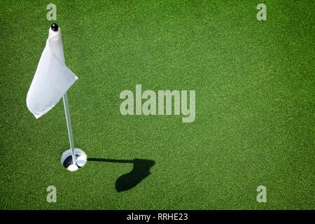 Two golf balls sit inside cup on golf course putting green with flag. Stock Photo