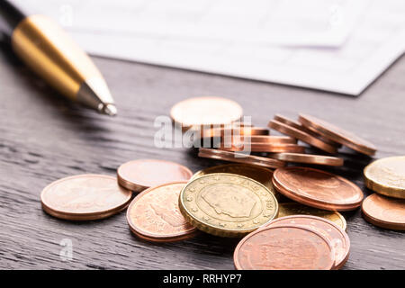 Stack of euro euro coins on old black wooden table. Pen and accounting documents with numbers. Payment planning utility bills Stock Photo