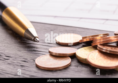 Stack of euro euro coins on old black wooden table. Pen and accounting documents with numbers. Payment planning utility bills Stock Photo