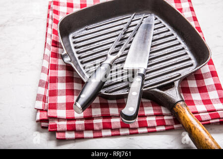 Empty grill pan on marble table with red tablecloth knife and fork. Stock Photo