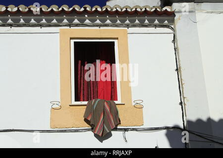 Blanket draped over the window sill, red curtains, yellow trim, Evora, Alentejo, Portugal Stock Photo
