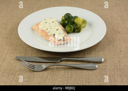 Baked salmon fillet with light cream sauce with capers and brussel sprouts in a light butter sauce on white plate with fork and knife Stock Photo