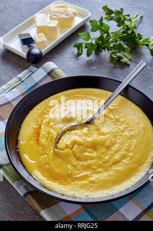 polenta with melting butter in a bowl on a napkin with silver spoon on a grey concrete table, vertical view from above Stock Photo