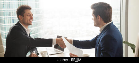 Horizontal image businessmen in suit handshaking sitting at modern office Stock Photo
