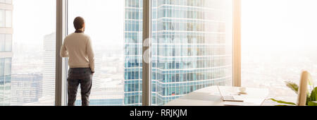 Horizontal image rear view businessman standing looking through panoramic window  Stock Photo