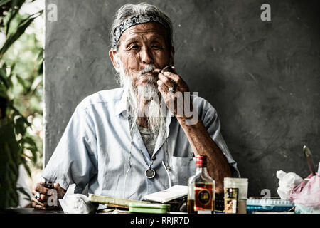 OSAKA - JAPAN - 20 FEBRUARY 2019. Portrait of an eldelry Japanese man smoking a pipe while on the table there is a bottle of rum and painting tools. J Stock Photo