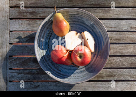Pears and apple cut on blue plate in sunlight on wooden table. Stock Photo