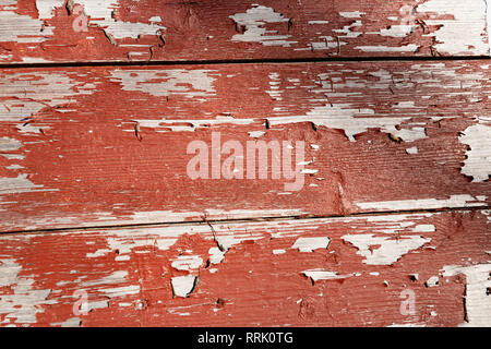 Red paint peeling of wooden wall in sunlight. Stock Photo