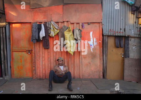 An exhausted worker in a dockyard in Mazgaon area, in Mumbai, India, relaxes in front of his living quarters, a rudimentary, if colorful,  tin shack Stock Photo