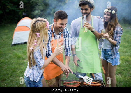 Happy group of friends making a barbecue together outdoors in the nature Stock Photo