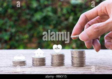 Savings money for life future concepts. Hand holding coin over stacked coins, car, house, healthy on stacking coins. Depicts saving for wealth and lif