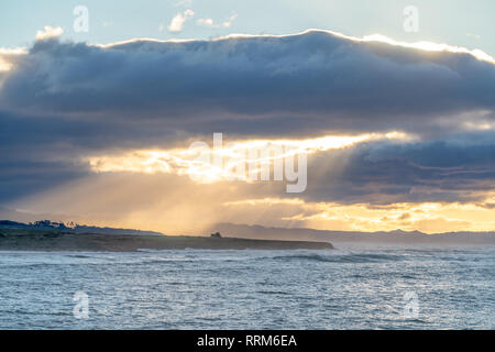 Clouds part during a sunrise along the California coast, creating stunning light rays through the ocean spray. Stock Photo