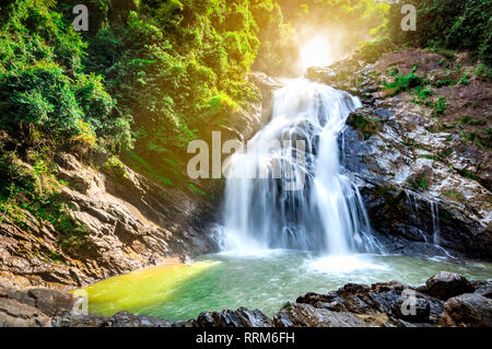 Beautiful waterfall at the mountain with blue sky and white cumulus clouds. Waterfall in tropical green tree forest. Waterfall is flowing in jungle. N Stock Photo