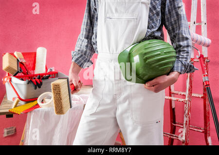 Young Caucasian house painter worker in white work overalls, holds the brush with your hands. Construction industry. Work safety. Stock Photo