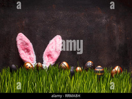 Cute Easter scene with pink rabbit ears and eggs hiding in green grass Stock Photo