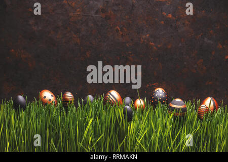 Black and golden Easter eggs in a row on green grass, space for your text Stock Photo